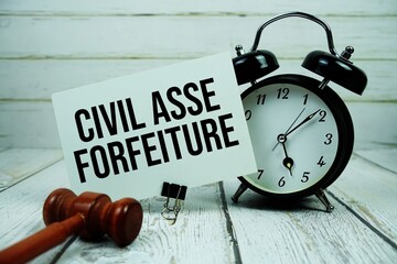 Civil Asset Forfeiture text on paper card with alarm clock and wooden judge gavel on wooden background