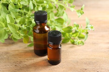 Essential oil in bottles and oregano twigs on wooden table, closeup