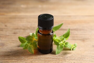 Essential oil in bottle and oregano twigs on wooden table, closeup