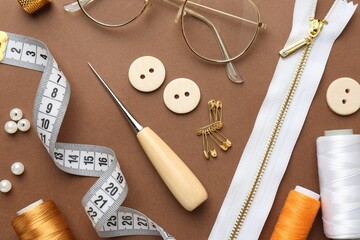 Flat lay composition with different sewing supplies and glasses on brown background