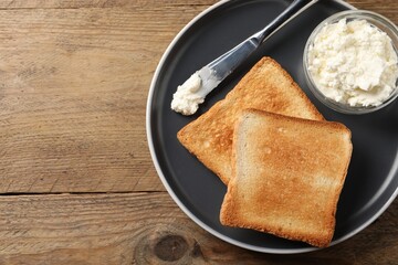 Delicious toasted bread slices with cream cheese and knife on wooden table, top view. Space for text