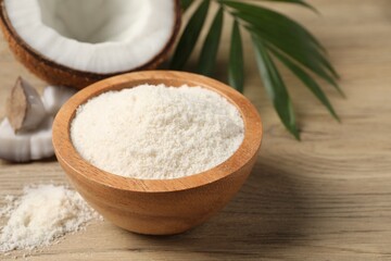 Fresh coconut flour in bowl, nut and palm leaf on white wooden table, closeup
