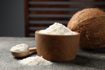 Coconut flour in bowl, spoon and fresh fruit on grey table, closeup