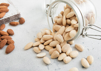 Glass jar with healthy raw almond whole and peeled nuts on white kitchen table.Macro.