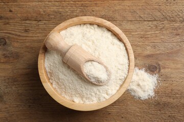 Organic coconut flour in bowl and scoop on wooden table, top view