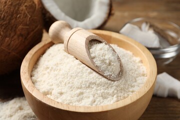 Coconut flour in bowl and scoop on wooden table, closeup