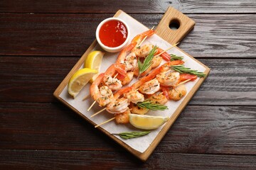 Delicious grilled shrimp skewers served with sauce and lemon on wooden table, top view