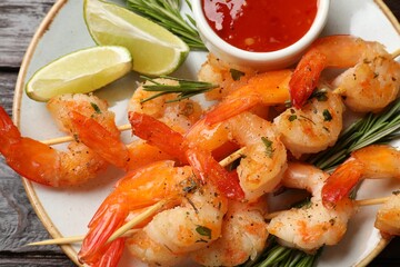 Delicious grilled shrimp skewers served with sauce and lime on wooden table, top view