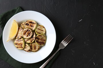 Tasty grilled zucchini slices served on black textured table, flat lay. Space for text