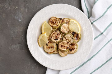 Tasty grilled courgette slices with lemon on grey textured table, top view