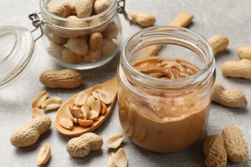 Tasty peanut butter in jar and groundnuts on grey textured table