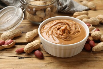 Tasty peanut butter in bowl and groundnuts on wooden table