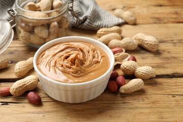 Tasty peanut butter in bowl and groundnuts on wooden table