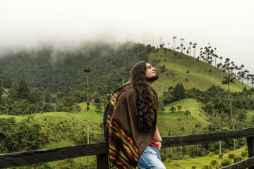 young latin man with long hair traveling to a wax palm forest in Colombia called cocora valley wearing an andean weaving ruana
