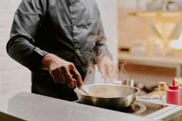 Medium close up of unrecognizable male hand stirring mushrooms in frying pan gently