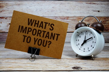 What's important to you? text on paper card with alarm clock on wooden background