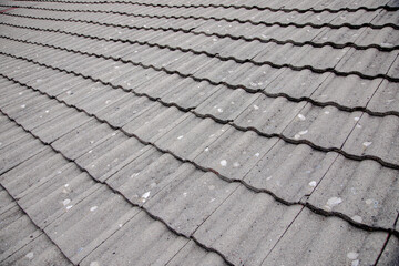 A close-up view of a weathered, corrugated grey rooftop with visible wear and patches, showcasing the texture and pattern of aged roofing material, ideal for backgrounds and architectural themes.