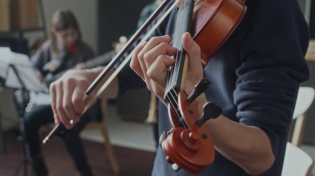 Tilt up view of teenage student playing violin during music lesson at school, kids practicing in background