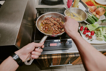 High angle shot of unrecognizable male hands holding pan and spoon while stirring bacon frying in...