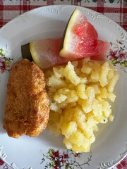 Delicious home-cooked meal with crispy fried fish, potatoes, and fresh pickled watermelon on a vintage decorative plate