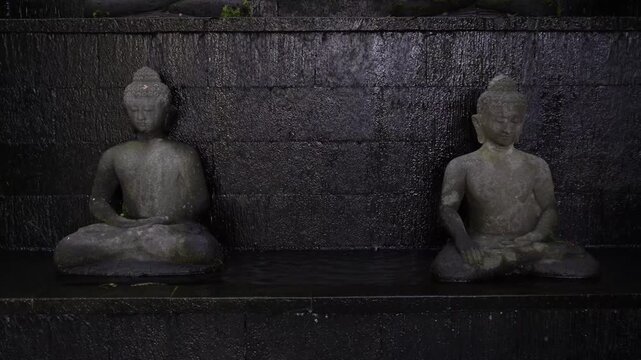 Stone statue of a Buddha figure meditating facing the front with waterfall on stone wall background. Bodhisattva Face. Concept for Vesak Day and Enlightenment Day. Empty blank copy text space