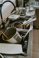Heap of dirty crockery in kitchen sink after cooking dinner by chef