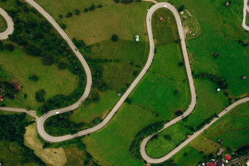 Fototapeta premium Aerial view of the road passing through the mountain and green forest. Curve asphalt road on mountain.