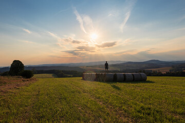 Man with backpack standing on grass bale at sunset. Natural reserve Novohradske mountain, Czech landscape