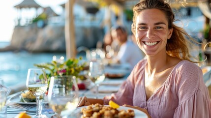 A woman with a broad smile is dining outdoors at a beautiful seaside location, enjoying a pleasant meal with wine, showcasing a sense of relaxation and joy.