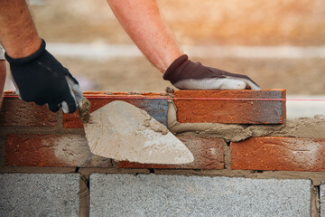 Construction Worker Using Trowel to Spread Mortar Between Red Bricks