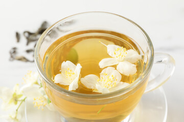 Aromatic jasmine tea in cup and flowers on table, closeup