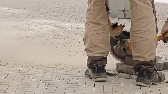 worker in overalls cuts paving slabs on construction site with grinder, slow motion