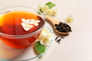 Hot jasmine tea in cup and flowers on white wooden table, closeup. Space for text