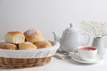 Delicious dough balls with powdered sugar in basket, tea, teapot and gypsophila flowers on white...