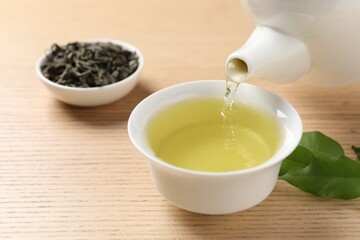 Pouring refreshing green tea into cup at wooden table, closeup