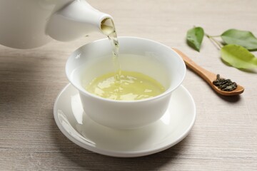 Pouring refreshing green tea into cup at wooden table, closeup