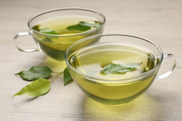 Refreshing green tea in cups and leaves on wooden table, closeup