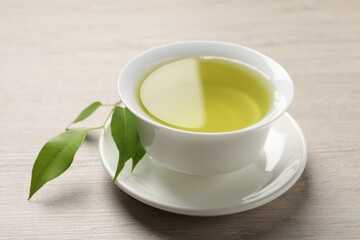 Refreshing green tea in cup and leaves on wooden table, closeup