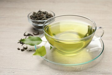 Refreshing green tea in cup and leaves on wooden table, closeup