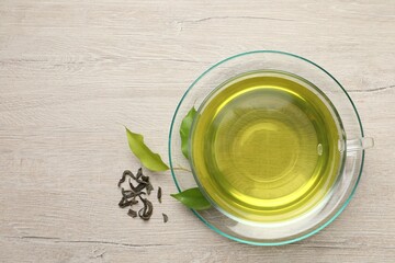 Refreshing green tea in cup and leaves on wooden table, flat lay. Space for text