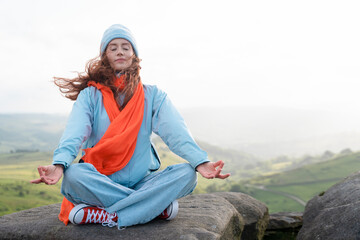 Woman Meditating on Misty Mountaintop in Blue Jacket and Orange Scarf