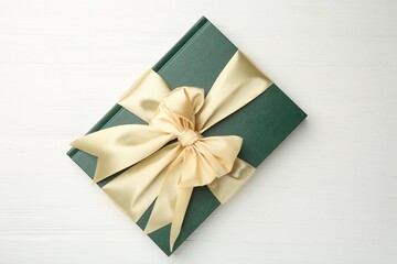 Hardcover book with ribbon as gift on white wooden table, top view