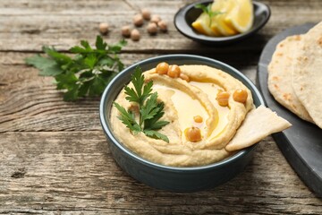 Delicious hummus with olive oil, chickpeas, parsley and pita in bowl on wooden table