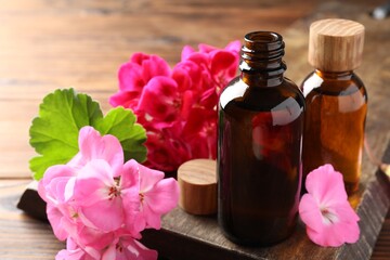 Geranium essential oil in bottles and beautiful flowers on wooden table