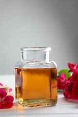 Bottle of geranium essential oil and beautiful flowers on white wooden table, closeup