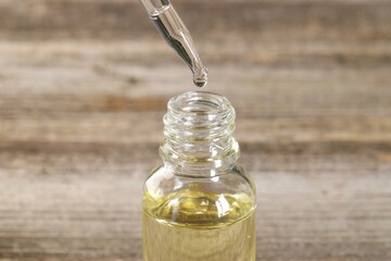 Dripping essential oil into bottle on wooden table, closeup