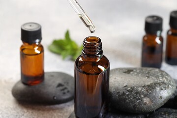 Essential oil dripping from pipette into bottle on table, closeup