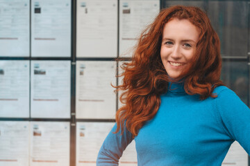 Smiling Woman With Red Hair Standing In Front Of Wall of White Papers
