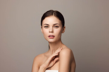 Beautiful young woman with hands on her face, posing on a gray background