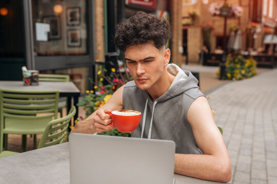 Young Man Working on Laptop and Drinking Coffee at Outdoor Cafe